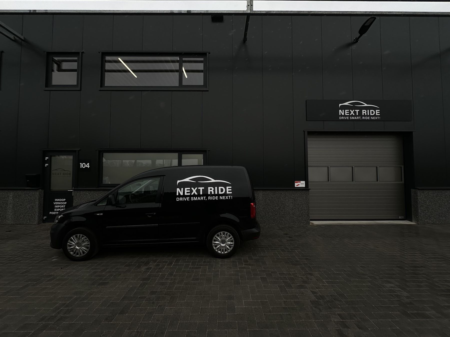 De zwarte gevel van Industrieweg 104 met de bus van Next Ride en het bord Drive smart, ride next!