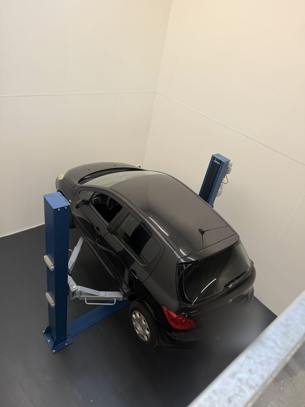 Een zwarte Peugeot op de blauwe tweekolomsbrug in de witte werkplaats, van bovenaf gezien