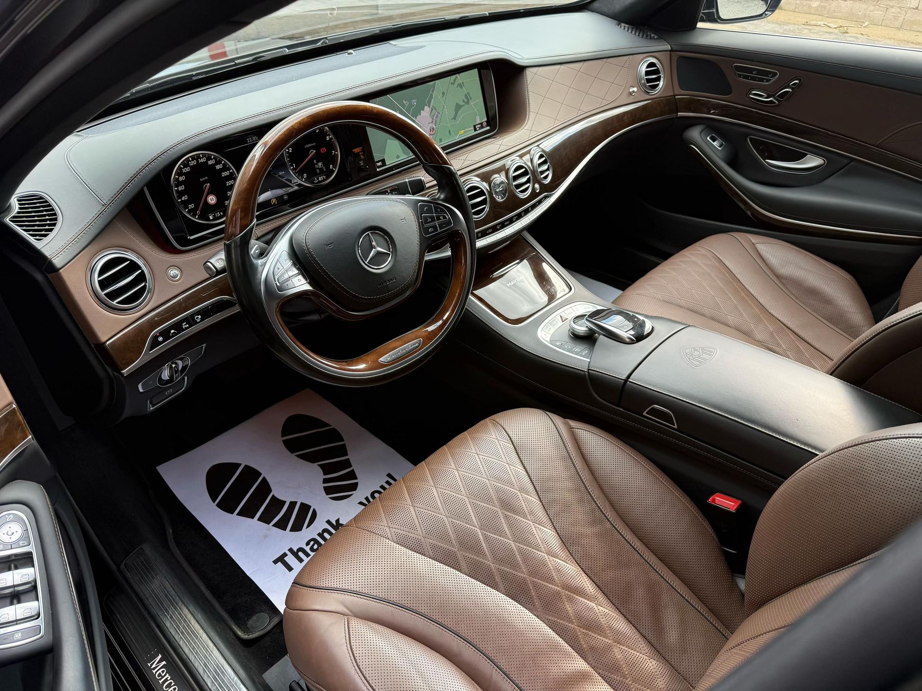 Het bruine gewatteerde leer in het interieur van de Maybach, met een papieren vloermat met Thank you