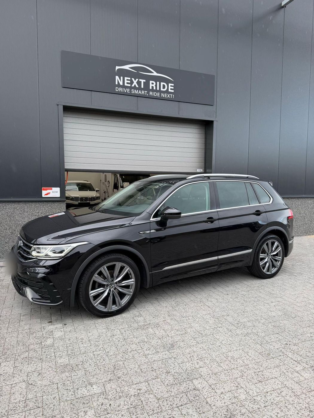 Een zwarte Volkswagen Tiguan voor de deur van Next Ride Automotive, met links het bordje RDW Erkend bedrijf